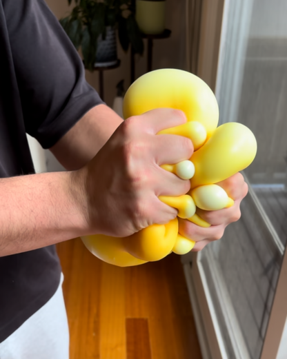 Person holding a yellow giant cheese stress ball on a wooden floor.